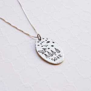 Silver pendant with birds soaring over a forest